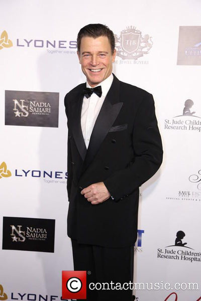 Man in a black tuxedo standing in front of a branded backdrop