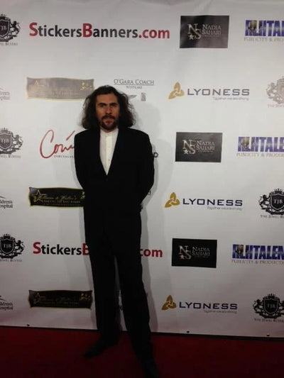 Man in a black suit standing in front of a branded backdrop with various logos.