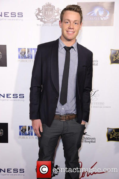 Man in formal attire standing in front of a branded backdrop