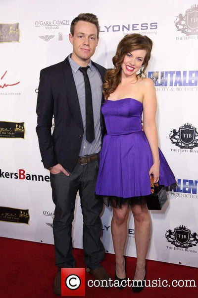 Man and woman posing on a red carpet event with a branded backdrop