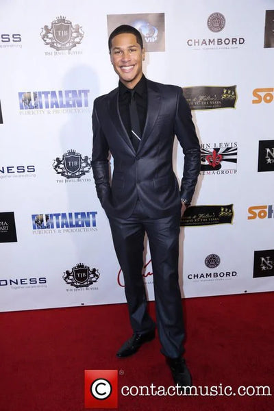 Man in a black suit standing on a red carpet with event branding in the background