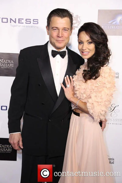 Man in tuxedo and woman in formal gown posing on a red carpet with event branding.