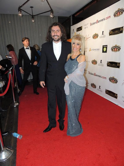 Man and woman on a red carpet event with a backdrop featuring logos.