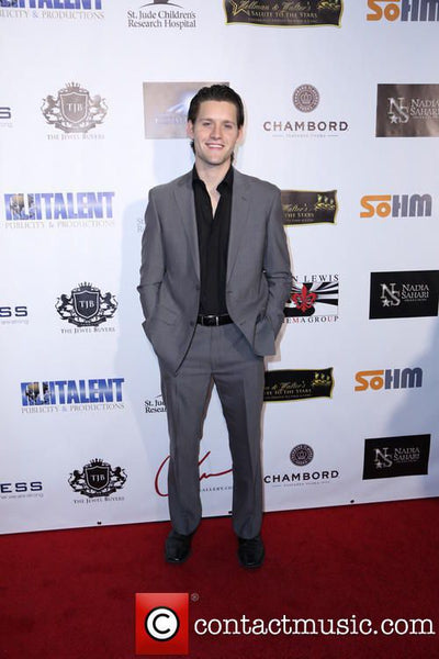 Man in a gray suit standing on a red carpet with a branded backdrop