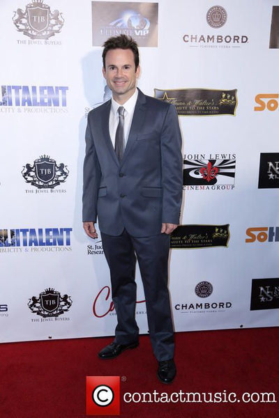 Man in a suit standing on a red carpet with event sponsor logos in the background