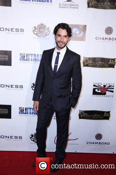 Man in a suit standing on a red carpet with event sponsor logos in the background