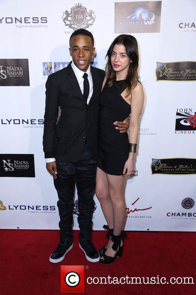 Man and woman posing on a red carpet with sponsor logos in the background