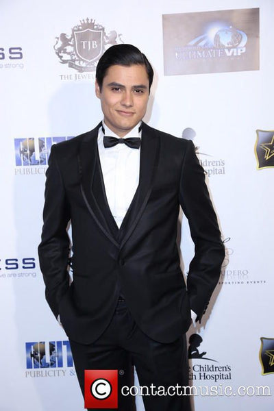 Man in a black tuxedo standing against a branded backdrop