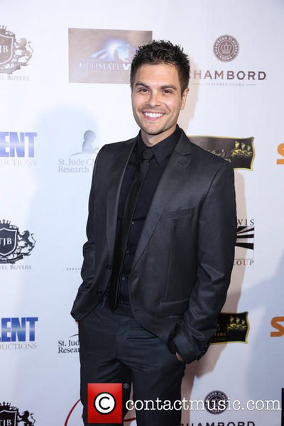 Man in a black suit standing in front of a branded backdrop