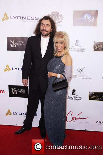Man and woman posing on a red carpet event with sponsor logos in the background