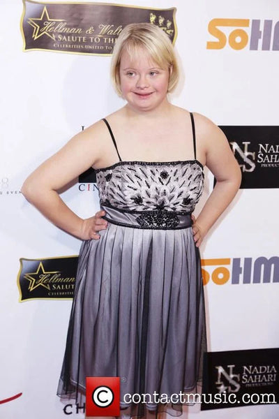 Person wearing a black and gray dress at an event with promotional banners in the background.