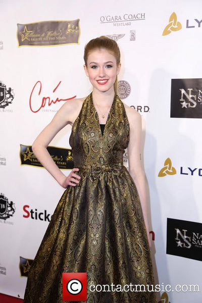Woman in a gold dress at an event with various logos in the background
