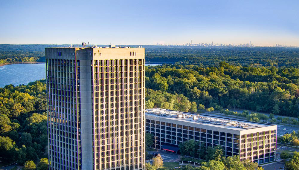 Tall office building with a surrounding green landscape and body of water.