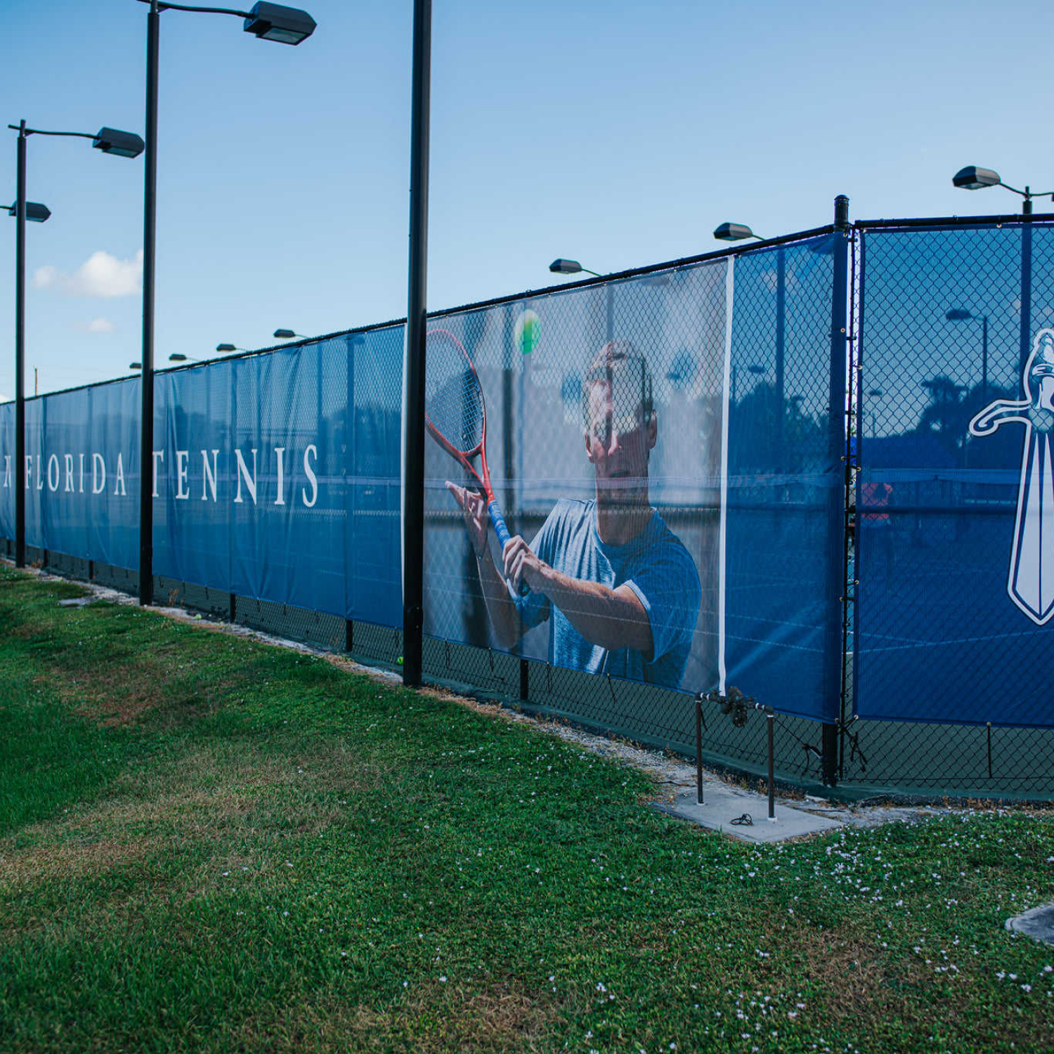 Tennis court with a player on a screen behind a fence, featuring 'Florida Tennis' branding.