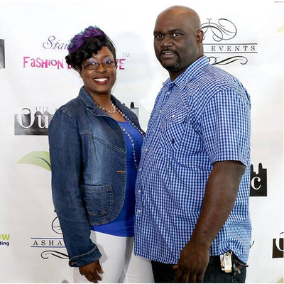 Two people standing in front of a promotional backdrop with logos and text.