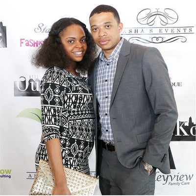 Two people posing together at an event with a branded backdrop
