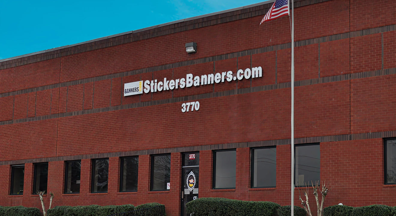 Red brick building with 'StickersBanners.com' sign and American flag on a clear day.