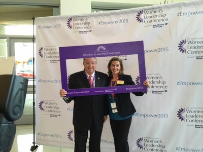 Two people holding a framed photo in front of a Women's Leadership Conference backdrop.